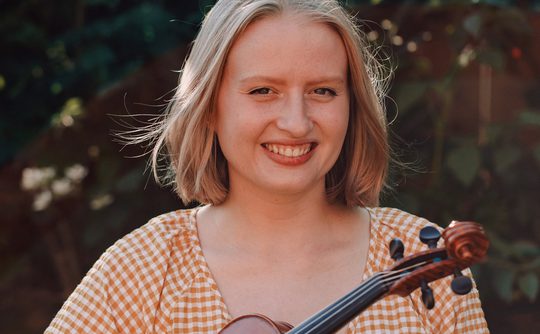 Woman smiling holding a violin - Benslow Music Course Tutor
